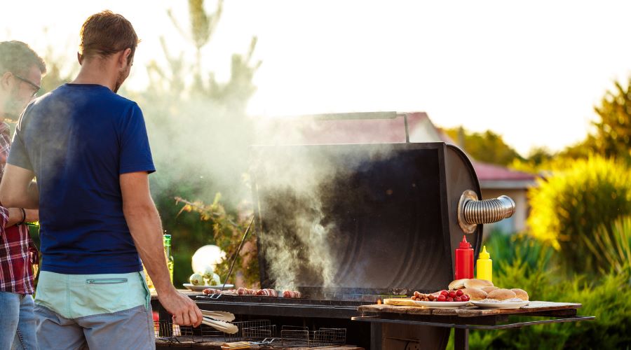 Zwei Männer grillen im Garten an einem Holzkohlegrill – Tipps für Anfänger zum perfekten Grillstart 2025.