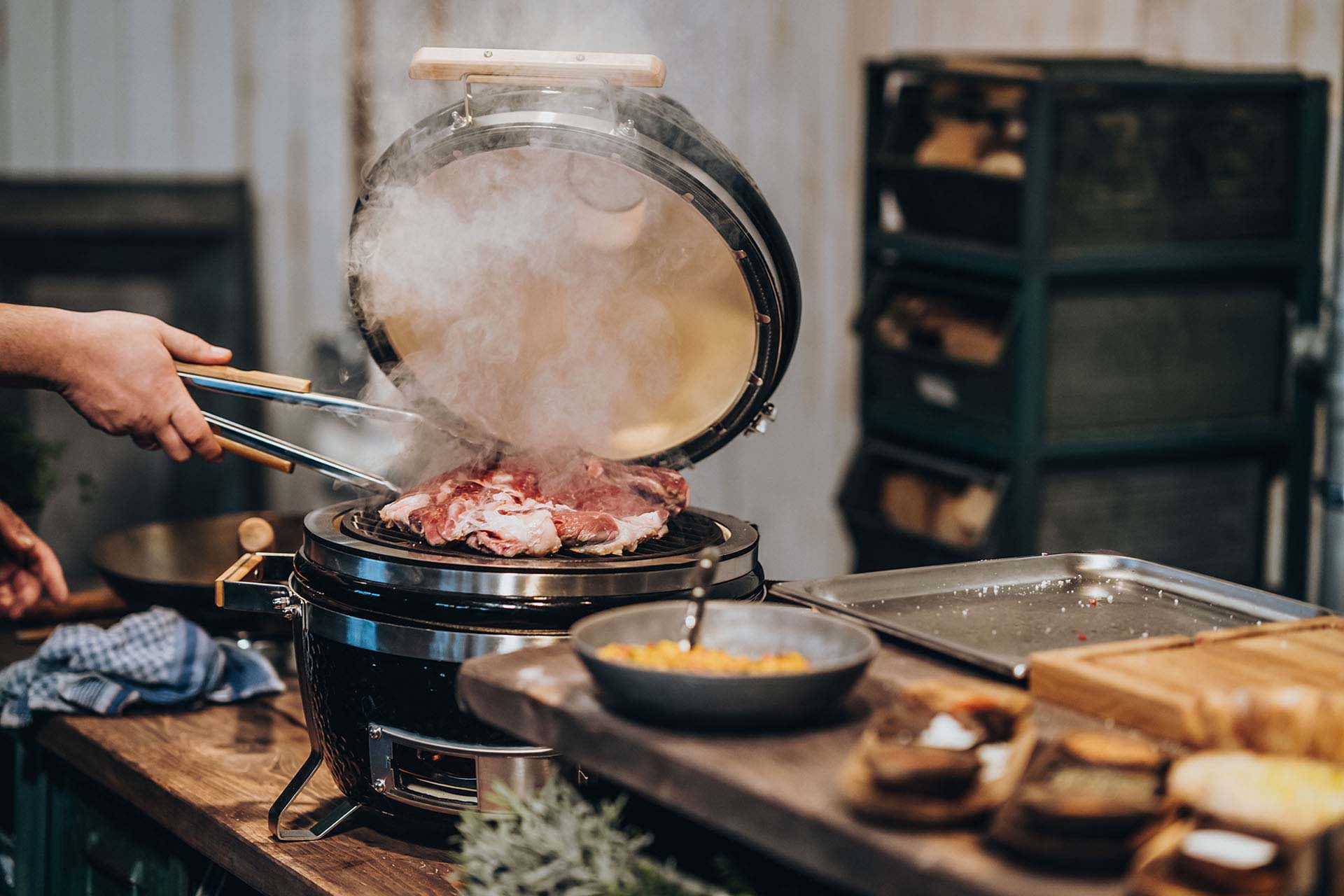 Ein Keramikgrill auf dem ein großes Stück Fleisch mit einer Zubehör Grillzange gewendet wird