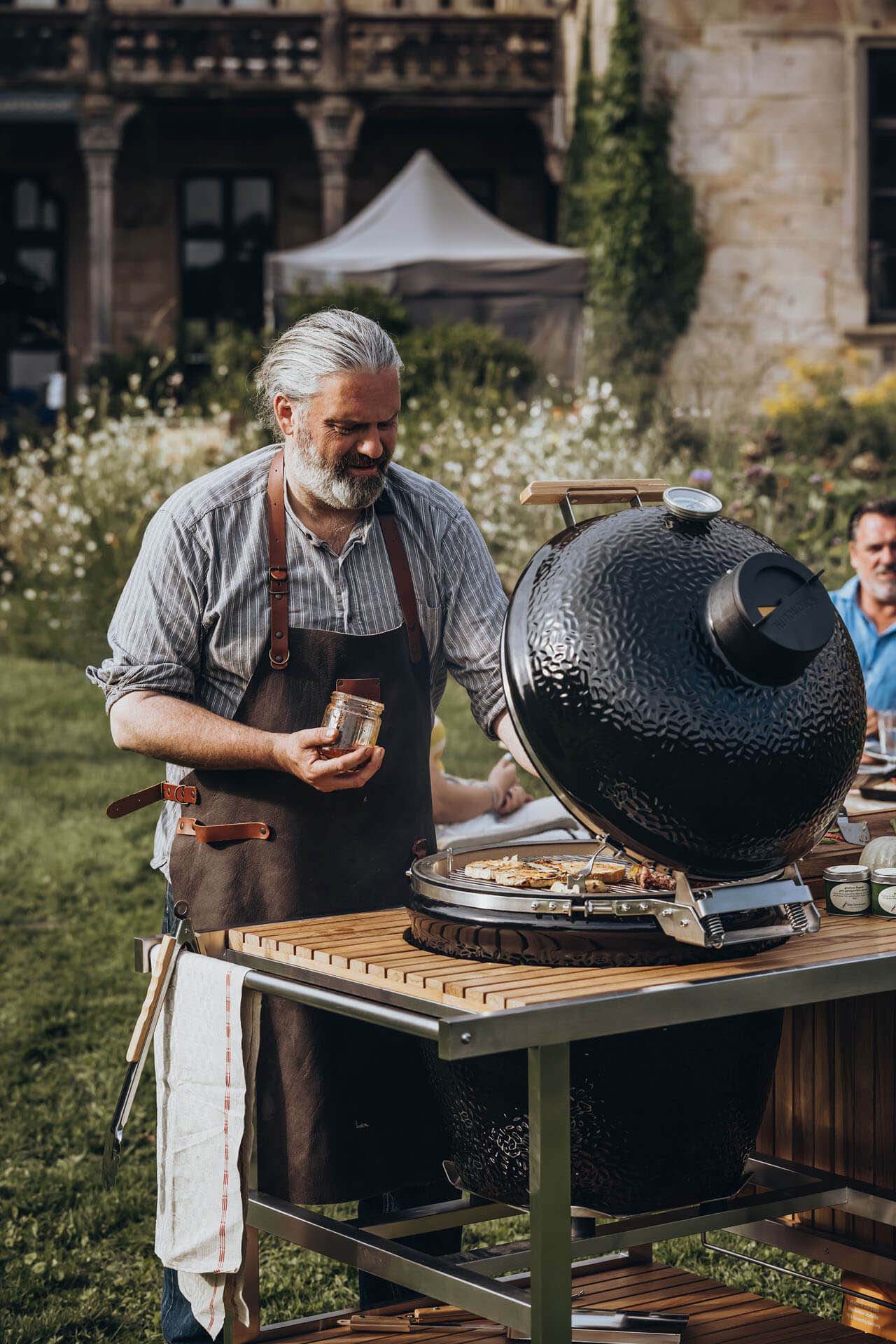 ein Mann vor einem voll belegten Keramikgrill am grillen