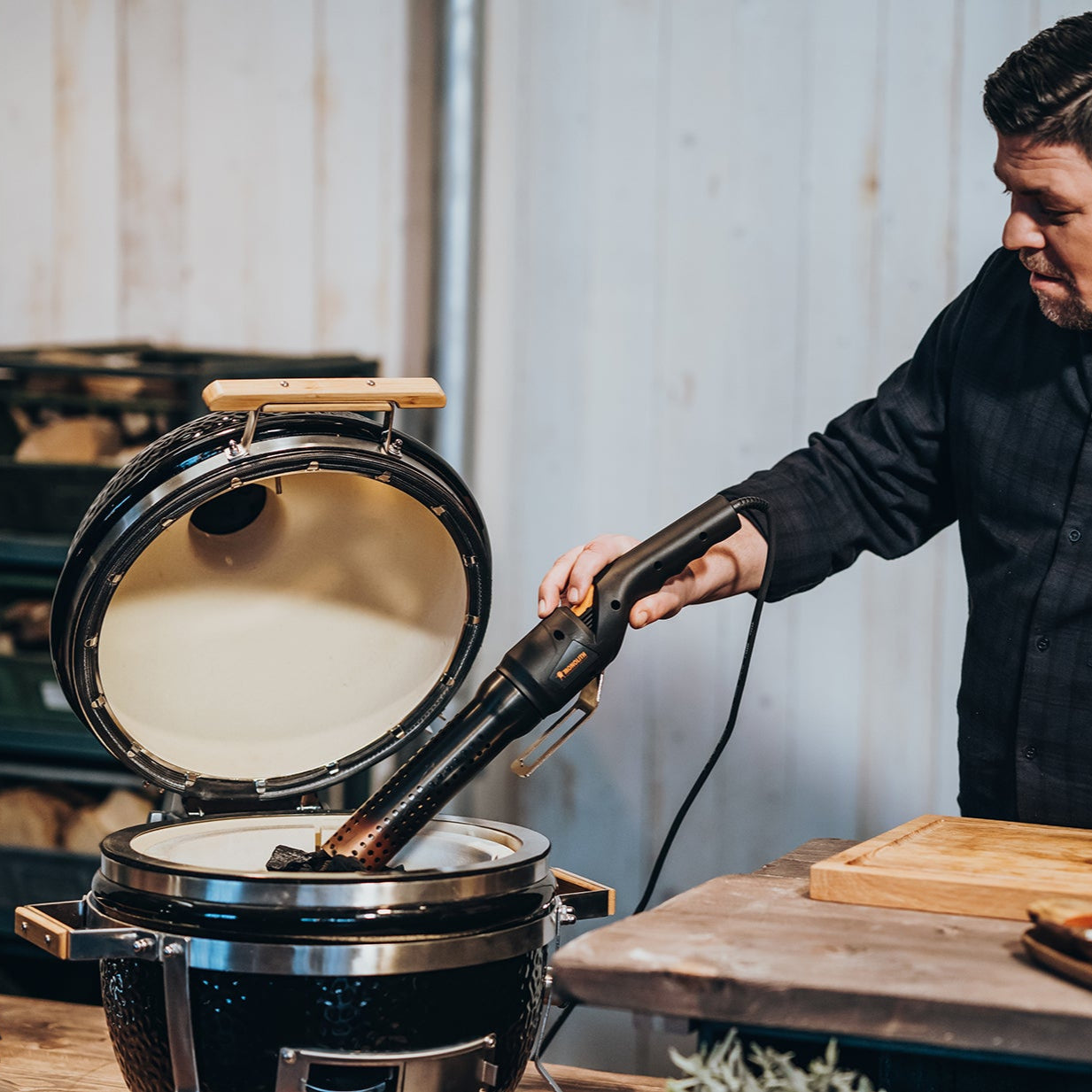 Grillmeister zündet Holzkohle im geöffneten Kamado-Grill mit einem elektrischen Grillanzünder