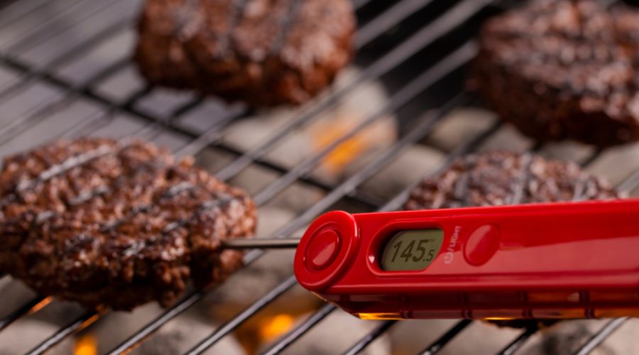 Digitale Grillthermometer misst die Kerntemperatur eines Burgers bei 145 °F direkt auf dem Grillrost über glühender Holzkohle.