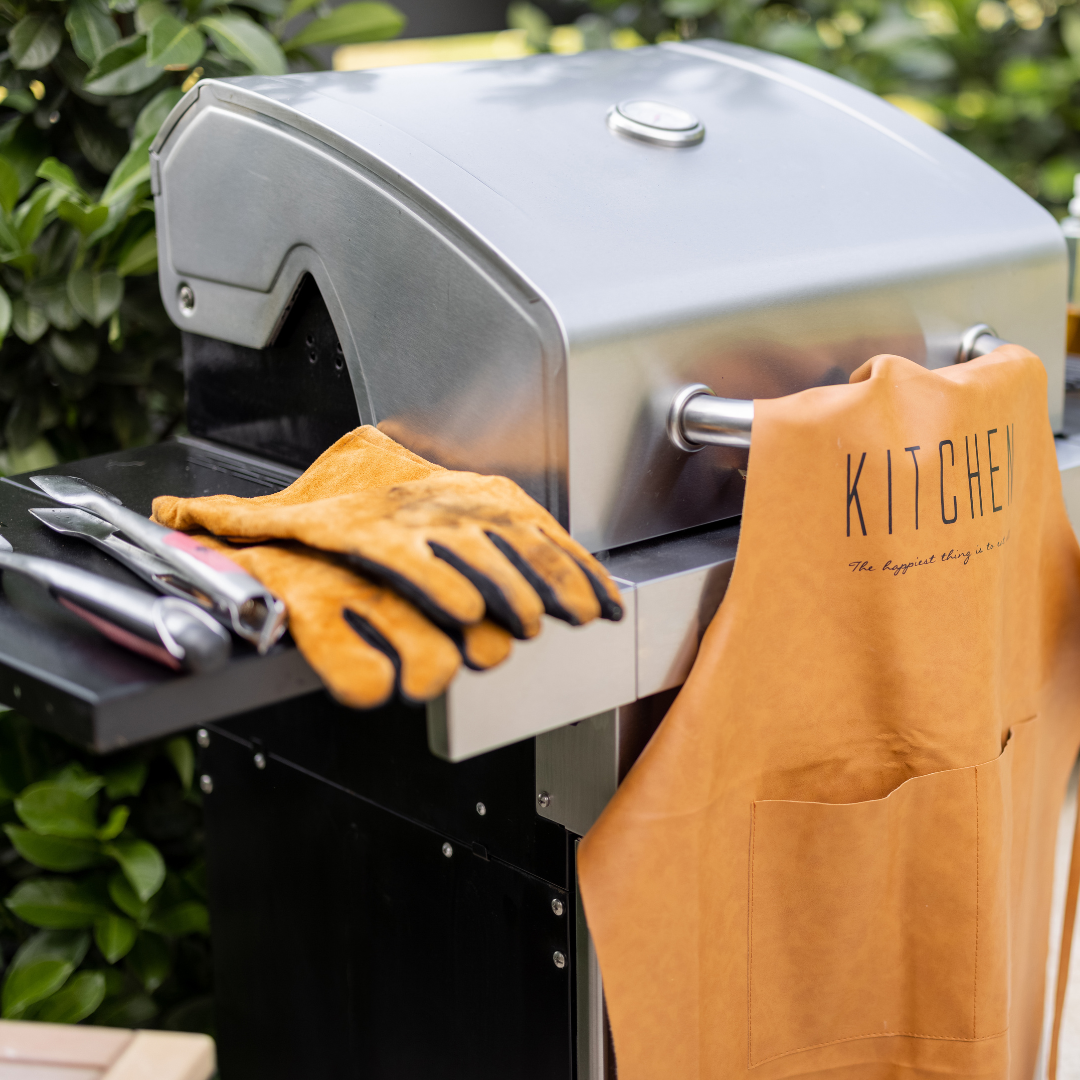 Verschiedene Grillutensilien wie Grillzange, Thermometer und Grillhandschuhe auf einem Tisch, bereit für das perfekte Grillerlebnis.